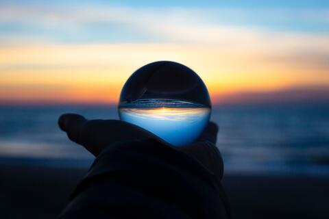 hand holding glass ball reflecting beach sunrise