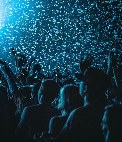 A photo of a crowd waving hands in the air in a burst of confetti