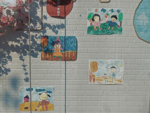 A photo of four children's drawings on a white brick wall